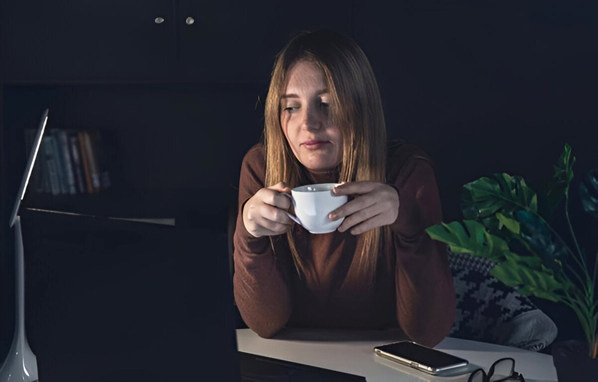 Žena večer sedí pri stole s pohárom v ruke, unavene sa pozerá na obrazovku laptopu – symbolizuje problémy so zaspávaním a nespavosť spôsobenú neskorou prácou
